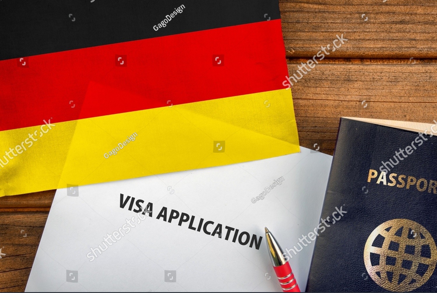 German flag beside a visa application form, passport and red pen on a wooden surface.